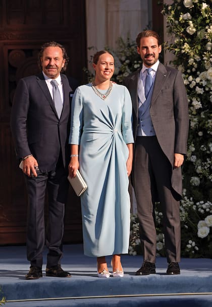 Philippos de Grecia, hermano de la novia, y su mujer, Nina Flohr, con looks perfectamente coordinados (ella llevó un modelo de Adam Lippe con drapeado lateral en azul pastel, que combinaba con el chaleco y la corbata de él), junto al padre de Nina, Thomas Flohr, fundador de VistaJet, la flota de jets privados más importante del mundo.