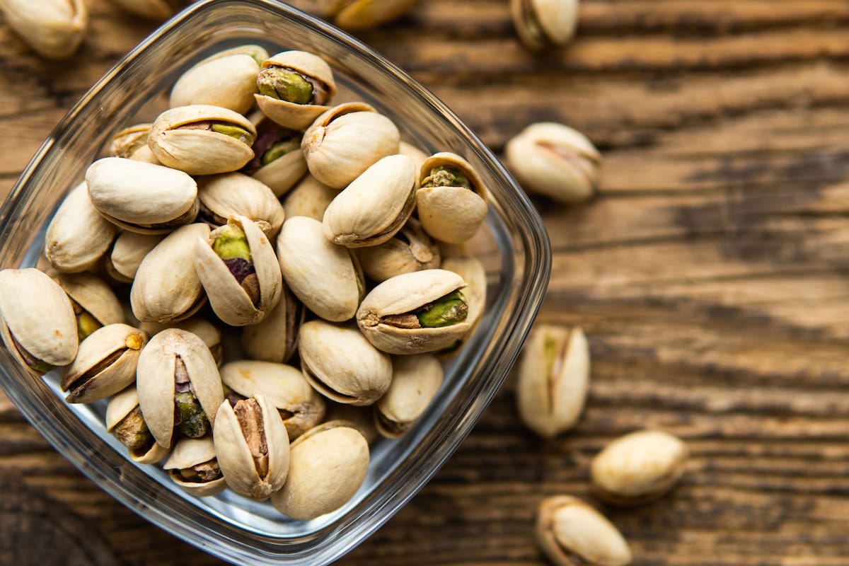 Pistachios in a small plate with scattered nuts of almonds around a plate on a vintage wooden table as a background. Pistachio is a healthy vegetarian protein nutritious food. Natural nuts snacks.