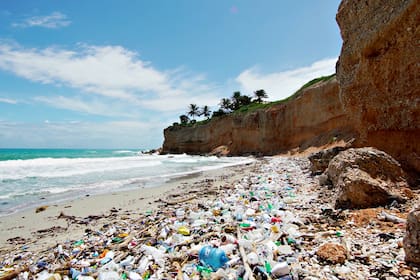 Plastic trash on the sea sandy white beach. Rocky coast of the peninsula in the ocean. Sea waves on a sunny day.
