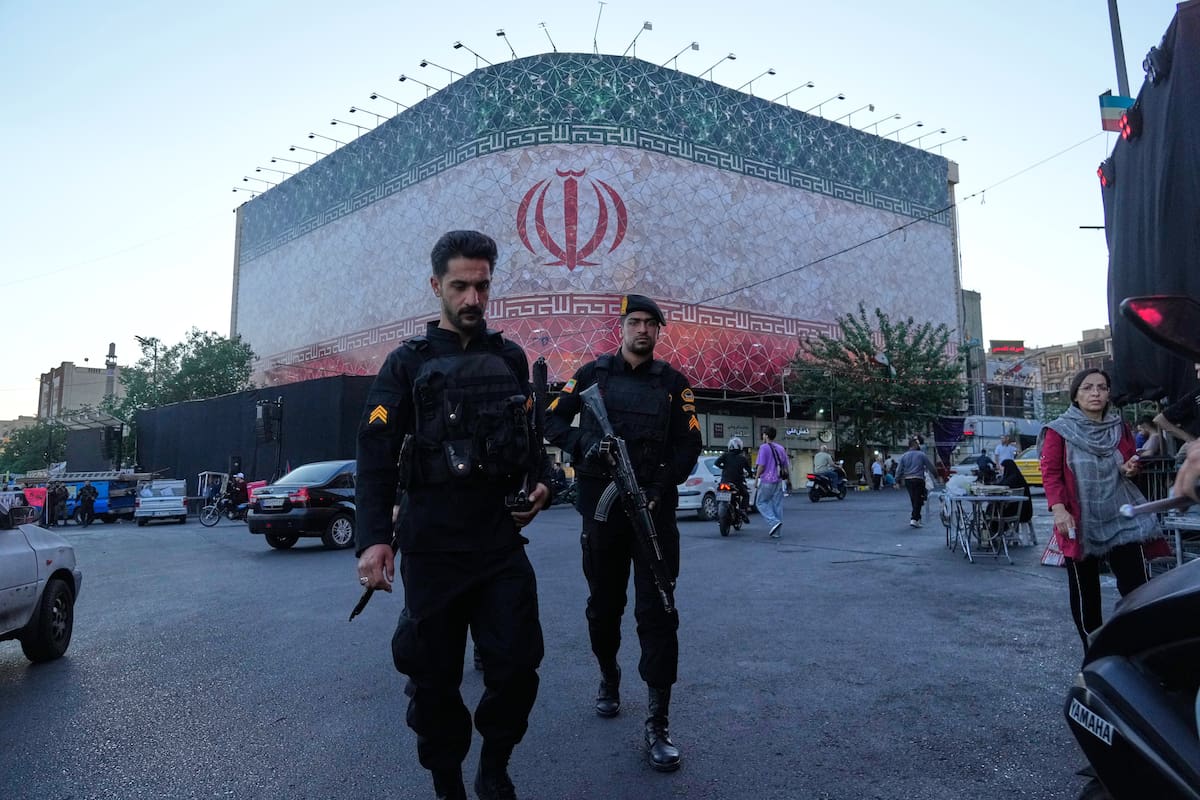 Policías caminan frente a una enorme pancarta con la bandera iraní en la plaza de la Revolución Islámica en Teherán, Irán, el domingo 14 de junio de 2026.