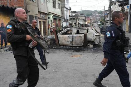 Policías pasan junto a un coche quemado que fue utilizado como barricada durante el operativo policial, en Río de Janeiro, el martes 28 de octubre de 2025