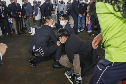 Policías someten contra el piso a un hombre que al parecer lanzó una bomba de humo durante la visita del primer ministro Fumio Kishida a un puerto en la prefectura de Wakayama, oeste de Japón, el sábado 15 de abril de 2023.