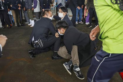 Policías someten contra el piso a un hombre que al parecer lanzó una bomba de humo durante la visita del primer ministro Fumio Kishida a un puerto en la prefectura de Wakayama, oeste de Japón, el sábado 15 de abril de 2023.