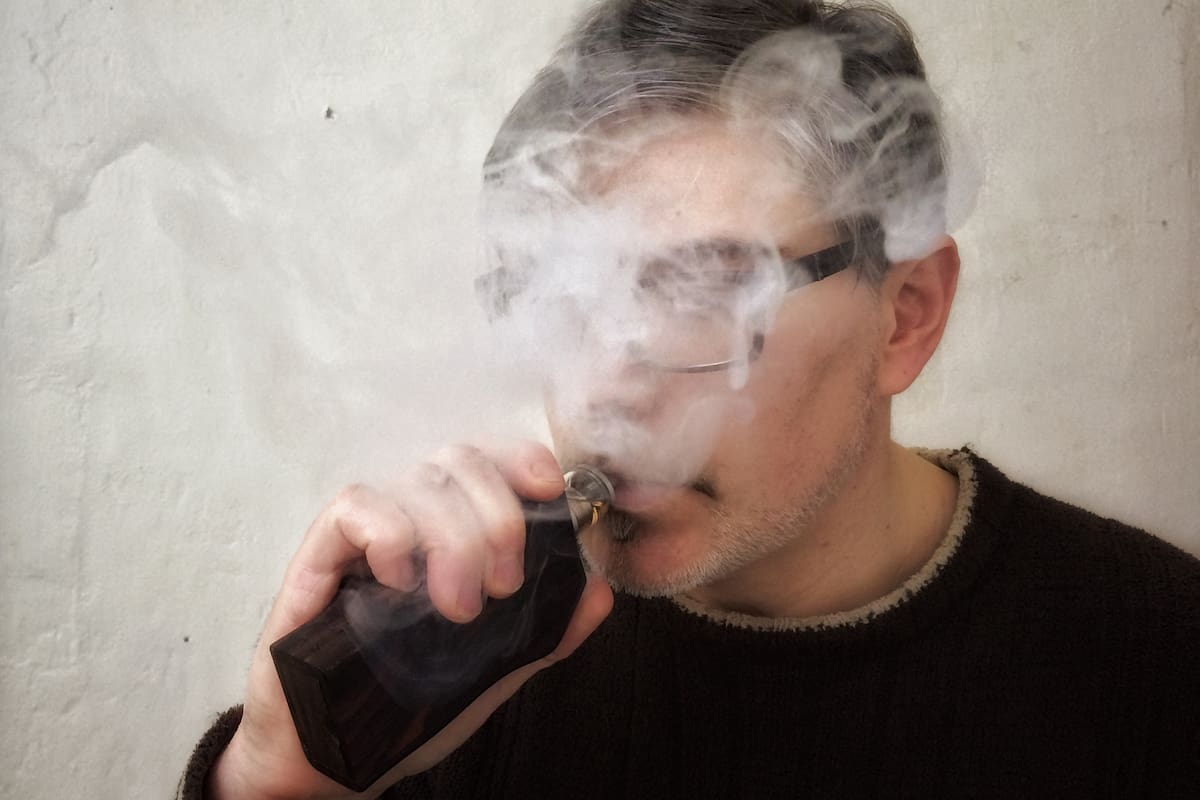 Portrait of a man vaping with face partially obscured by vapour.