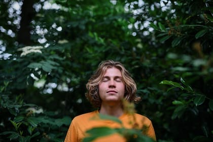 Portrait of happy man standing in forest, with closed eyes, smiling.