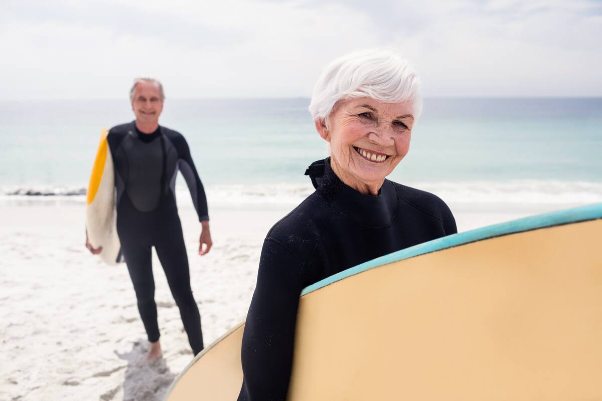 Portrait of senior couple in wetsuit holding surfboard on beach on a sunny day