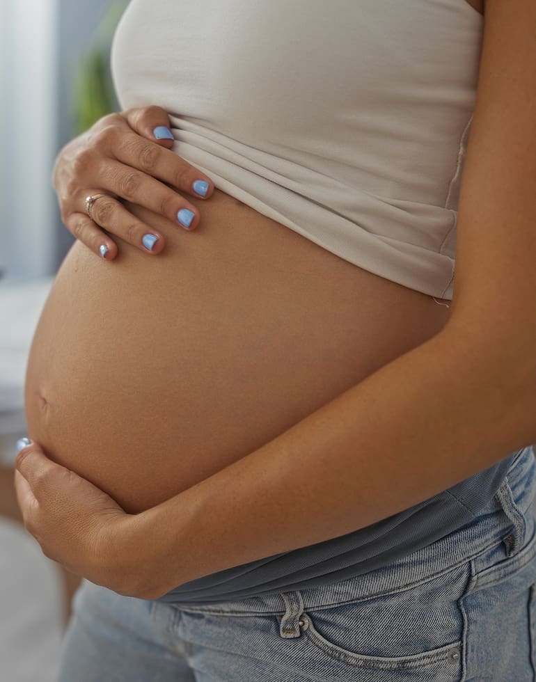 Pregnant woman with belly in a clinic room while doctor sits with a tablet providing medical consultation