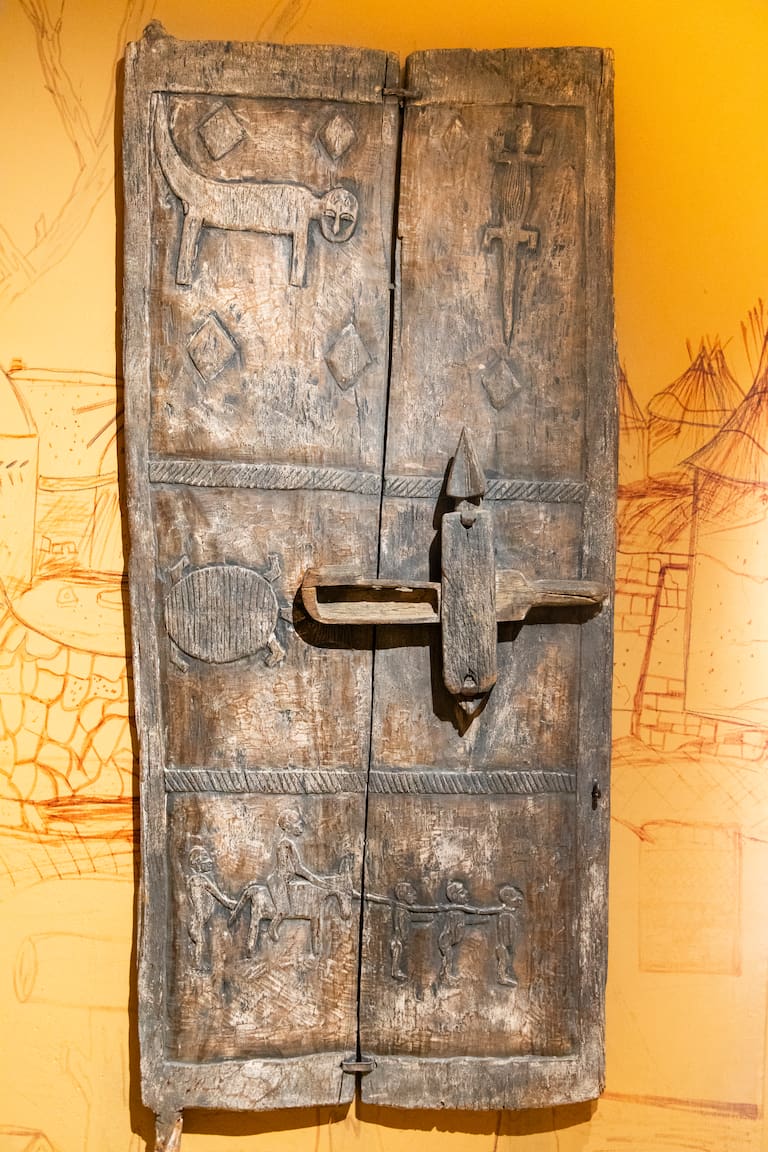 Puerta de granero tradicional de África Occidental, tallada en madera, con su mecanismo de cerradura de madera estilizado original. Forma parte de la extensa colección de objetos del patrimonio africano expuestos en el Museo Kurá Hulanda en Willemstad, Curazao.