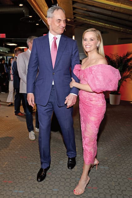 Reese, en un guiño al estreno, lució un vestido rosa chicle de encaje
de Monse, de escote Bardot y con flores aplicadas. Su amor,
el financista Oliver Haarmann, acompañó con traje azul y corbata rosa a
juego
