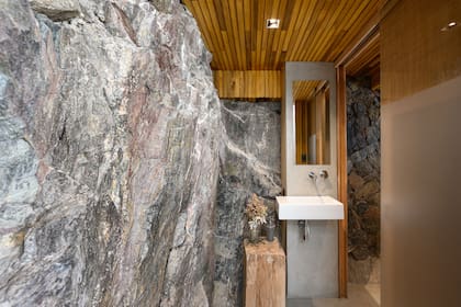 Repitieron el techo de paraíso y, con microcemento alisado, marcaron el sector para el espejo y una bacha. Mientras que el lateral izquierdo es de roca natural, la pared derecha está revestida con rocas sueltas.