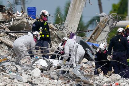 Rescatistas levantan una lona que contiene restos humanos recogidos en el sitio del edificio residencial derrumbado