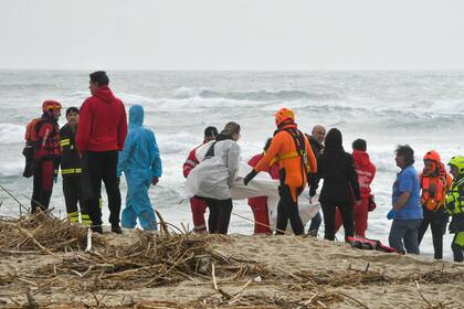 Rescatistas recuperan un cadáver de una playa cercana a Cutro, en el sur de Italia, el domingo 26 de febrero de 2023, después de que un bote de migrantes se partió en un mar picado. (AP Foto/Giuseppe Pipita)