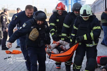 Rescatistas ucranianos transportando a una persona herida en una camilla tras un ataque aéreo contra la estación de tren de Dnipro