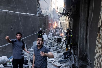 Rescatistas y bomberos apagaron un incendio en medio de la destrucción luego de un ataque aéreo israelí en la Ciudad de Gaza, el 5 de agosto de 2022. (Photo by Mohammed ABED / AFP)