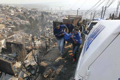 Rescatistas y vecinos llevan el cuerpo de una víctima del fuego