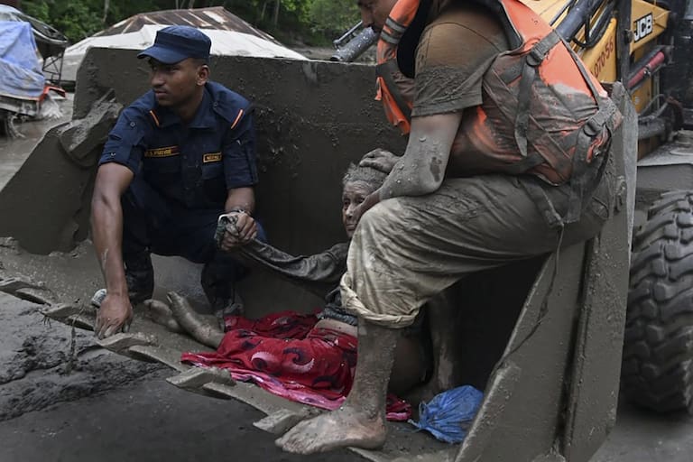 Rescue personnel use an excavator to carry a person affected by flash floods at Devghat in Nepal's Nuwakot district on August 26, 2026. Massive flooding killed eight people in Nepal on August 26, as Chinese state media reported "major casualties" from a mudslide at a Tibet trade hub on China's side of the nations' shared border. (Photo by Prakash MATHEMA / AFP)