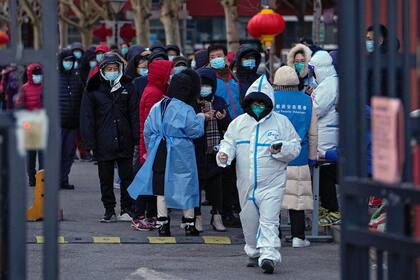 Residentes, con mascarilla para protegerse del coronavirus, esperan en fila para someterse a una prueba de detección del COVID-19 en un centro habilitado en el exterior de un bloque residencial en el distrito de Fengtai, en Beijing, el 26 de enero de 2022. (AP Foto/Andy Wong)