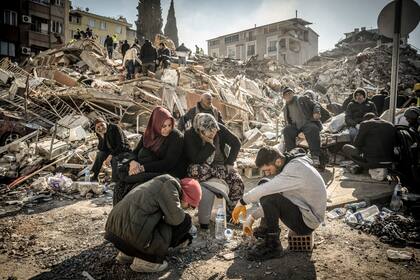 Residentes desplazados sentados cerca de su casa derrumbada mientras continúan las operaciones de rescate en Antakya, Turquía, el jueves 9 de febrero de 2023