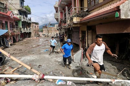 Residentes locales caminan junto a casas anegadas de lodo tras unas inundaciones repentinas en Devighat, municipio de Bidur (distrito de Nuwakot, Nepal), el 27 de agosto de 2026 (Prabin Ranabhat/ AFP)