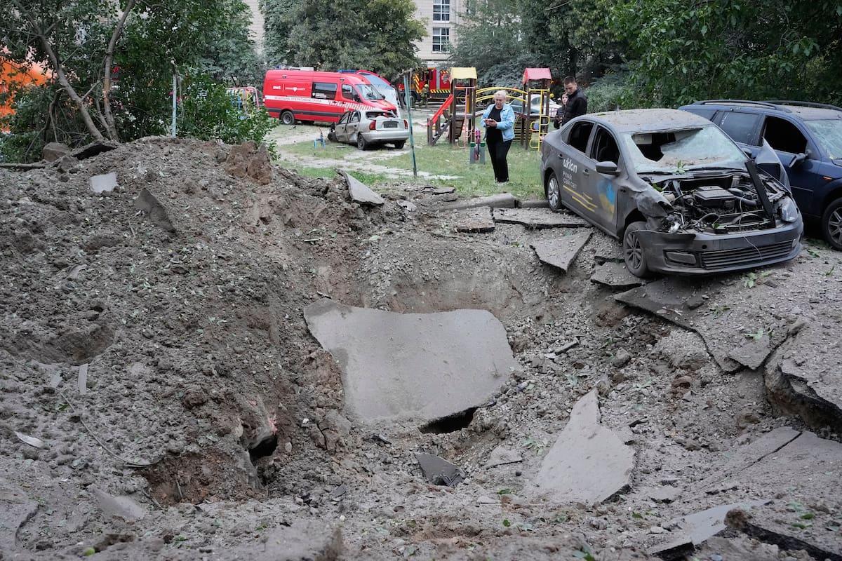 Residentes locales permanecen cerca de un cráter y de automóviles dañados por un ataque con misiles rusos en Kiev, Ucrania