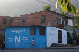 Residentes pasan frente a un cartel electoral del partido Nuevas Ideas que promueve la reelección del presidente Nayib Bukele en Soyapango, El Salvador, el martes 28 de febrero de 2023.