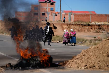 Residentes pasan junto a la policía cerca de barricadas levantadas por manifestantes antigubernamentales en una ruta en El Alto