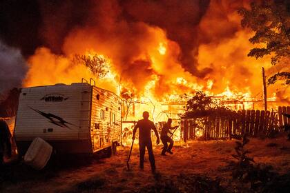 Residentes trabajan para impedir que el fuego de una vivienda en llamas se extienda a una casa cercana mientras el incendio 6-5 arde en la comunidad de Chinese Camp del condado de Tuolumne, California