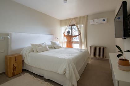 Respaldo de cama blanco sobre pared del mismo color, un bloque de madera natural como mesa de noche y aplique de pared (Huup).