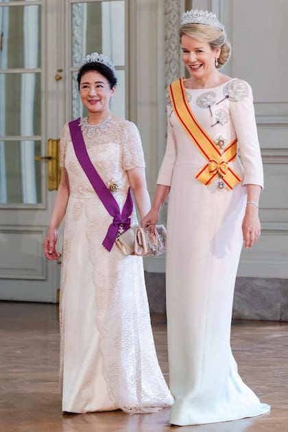 Masako lució un traje con bordados y superposición de encaje que complementó con la Tiara de Diamantes Madreselva, que perteneció a la princesa Chichibu, tía abuela del emperador. La Reina eligió un diseño a medida de Armani Privé, con sutil homenaje a sus invitados: el escote incluía bordados de paipáis típicos japoneses (abanicos rígidos de mano) y flores de loto en lentejuelas. Se coronó con la Tiara de las Nueve Provincias
