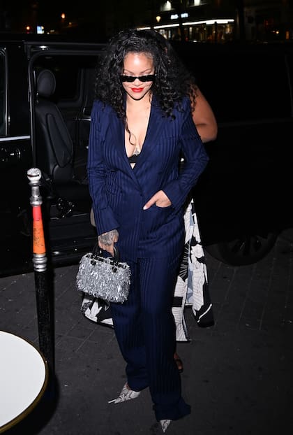 Rihanna fue a cenar al restaurante César de París después de asistir al concierto de Céline Dion. La cantante y empresaria lució un traje azul marino de rayas compuesto por una chaqueta cruzada y pantalones amplios. Completó el conjunto con stilettos de estampado serpiente, gafas de sol estrechas en color negro, un bolso plateado con brillo y un bralette negro de encaje