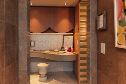 Rincón de trabajo resuelto en el pasillo que va del estar al dormitorio, con escritorio curvo empotrado de melamina Gris Tapir (Faplac), banco "Ronda" (Par en Par), alacena en melamina Terracota (Faplac) y revestimiento de porcelanato Cesky Ivory (San Lorenzo Design) sobre la pared.