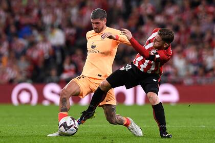 Rodrigo de Paul, de regreso a la titularidad tras casi un mes, forcejea con Muniain por la pelota, en el 1-0 de Atlético de Madrid como visitante de Bilbao por la liga de España.