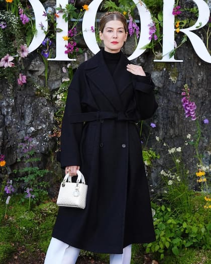 Rosamond Pike optó por un abrigo negro de lana con cinturón incorporado, jersey de cachemir a tono, pantalones blancos de seda y zapatos con plataforma.