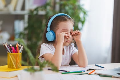 sad little girl, schoolgirl wearing headphones, uses laptop to study at home. child is bored to learn and gain knowledge remotely. student wants to go to school. digital concept e-learning.