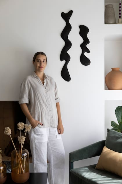 Sara Plazibat, se apoya en el frente de chimenea que cerraron para colgar la obra en madera de kiri de Agustín Leiro y crear nichos para objetos decorativos, como los jarrones de arcilla (Philippa Deco Boutique).