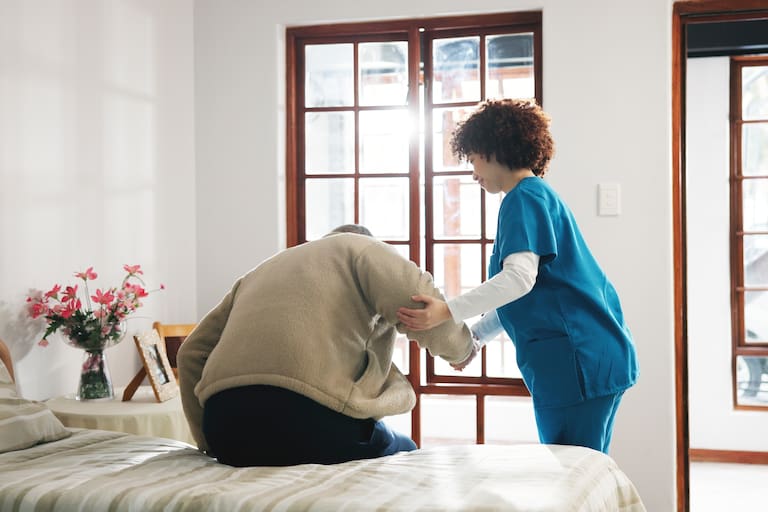 Senior man, caregiver or helping patient on bed for assisted living or support in retirement home. Male person, nurse or assistance in bedroom with client for elderly care or nursing in old age house