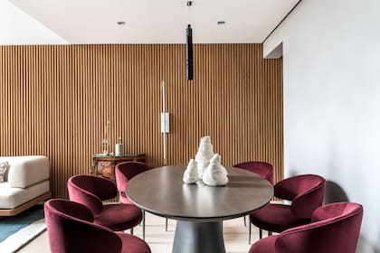 Siguiendo la altura del comedor, el revestimiento de pared (MAB Mobile Marcenaria) enchapado en madera de freijó avanza hacia el living. Lámpara de techo (dsgnselo).