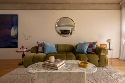 Sillón de tres módulos al estilo del modelo ‘Camaleonda’, diseñado en los 70 por el italiano Mario Bellini, tapizado en pana verde, con almohadones (De Levie). Mesa de centro de mármol Arabescato, diseñada por Vara Estudio y ejecutada por Piedra. Espejo ojo de pez (Barn BA).