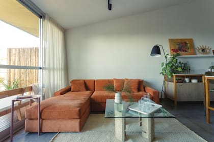 Sillón en L en pana naranja con tratamiento antimancha (Baume); banqueta de hierro esmaltado (Taller A Prima) y alfombra de lana cruda (Elementos Argentinos).