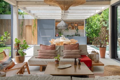 Sillones en madera y dúo de sillas tipo Jeanneret con esterilla. El mueble colgante junto a la parrilla se adaptó para exhibir plantas y objetos de madera que se disfrutan desde el estar.