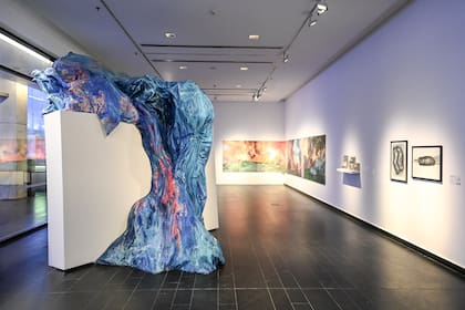 Simbiología: un tsunami de Paula Senderowicz en primer plano; detrás, dibujos de Leonel Luna y el monte en llamas en una gran pintura de Romina Orazi