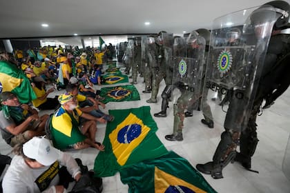 Simpatizantes del expresidente brasileño Jair Bolsonaro permanecen sentados frente a una hilera de policías militares dentro del Palacio de Planalto, luego de irrumpir al interior el domingo 8 de enero de 2023, en Brasilia, Brasil.