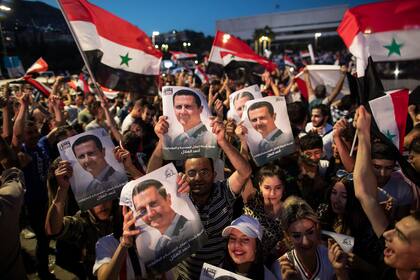 Simpatizantes del presidente Bashar Assad agitan banderas y sostienen retratos de él en la plaza Omayyad, en Damasco, Siria, después de que se anunciara que él gobernante ganó la reelección. (AP Fhoto/Hassan Ammar)