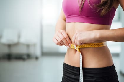 Slim young woman measuring her thin waist with a tape measure, close up