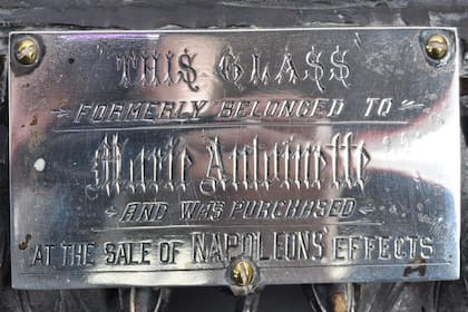 Sobre el marco hay una placa de vidrio que dice que el espejo perteneció a María Antonieta y que "fue adquirido en una venta de objetos de Napoleón"