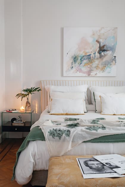 Sobre el respaldo a rayas (Estudio Ce), acuarela de la serie ‘Abstraída’. Almohadones y pie de cama estampado a mano (Mercedes Segura). Manta verde y funda de banqueta (Estudio Ce)