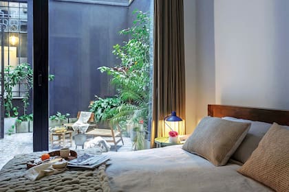 Las arquitectas combinaron los muebles que Iván trajo de Nueva York, como la cama de madera (Crate & Barrel) y la lámpara colgante de papel, con edredones, almohadones, manta tejida y cortinas de gasa teñida (Hilo Argentina) para aportarles calidez. Lámpara azul ‘Julia’ (Ikon).