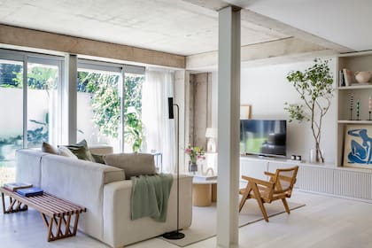 Sofá tapizado en género antimanchas con almohadones de terciopelo verde eucalipto y mueble de pared a pared laqueado en el mismo color del sofá (todo VK Home). Alfombra (Rug It).