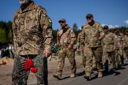 Soldados de la fuerza de defensa territorial de Irpin y del Ejército ucraniano llevan flores para depositar en las tumbas de sus compañeros caídos durante la ocupación rusa, en el cementerio de Irpin, a las afueras de Kiev, el 1 de mayo de 2022. (AP Foto/Emilio Morenatti)