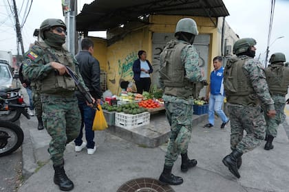 Soldados patrullan el perímetro de la prisión de Inca durante un estado de emergencia mientras un vendedor de alimentos trabaja en la acera en Quito, Ecuador, el 9 de enero de 2024, tras la aparente fuga de un poderoso líder de una pandilla de la prisión.